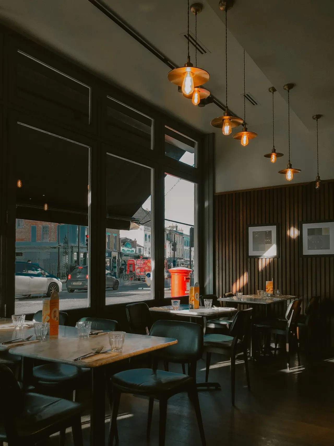 Salle de restaurant avec tables et suspensions près de fenêtres.